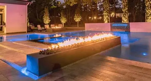 Fire bowls glowing beside a backyard pool at dusk
