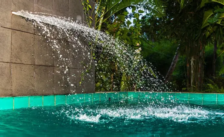 Backyard pool with a raised spa spilling water and a fire bowl